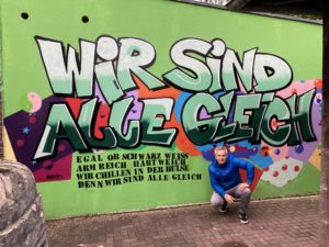 Johannes Veit vor einer Hülse Wand mit einem Graffit aus einem Workshop 2021